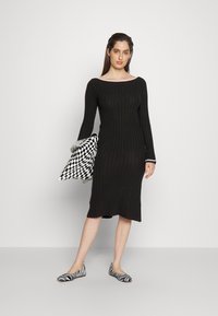 Μαύρο ριγέ φόρεμα με μακριά μανίκια και φαρδύ λαιμόκοψη, συνδυασμένο με τσάντα καρό σε μαύρο και λευκό και ριγέ επίπεδες γυναικείες παπούτσια.