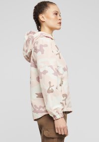 Lättviktsjacka med kamouflagemönster i rosa och krämfärger, med huva, elastiska ärmslut och sidoficka med dragkedja. Mjukt, vattentåligt material.