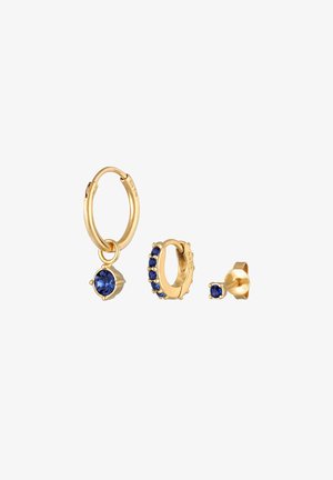 Goldfarbene Ohrringe mit einem großen blauen Kristallanhänger, einem Ring mit mehreren blauen Steinen und einem einfachen blauen Steckerohrring.