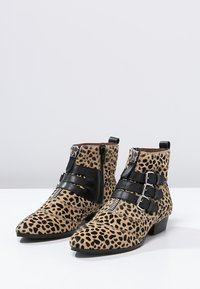 Leopard print ankle boots with black leather accents, featuring buckles and zippers, pointed toe, and low block heel. Soft texture.