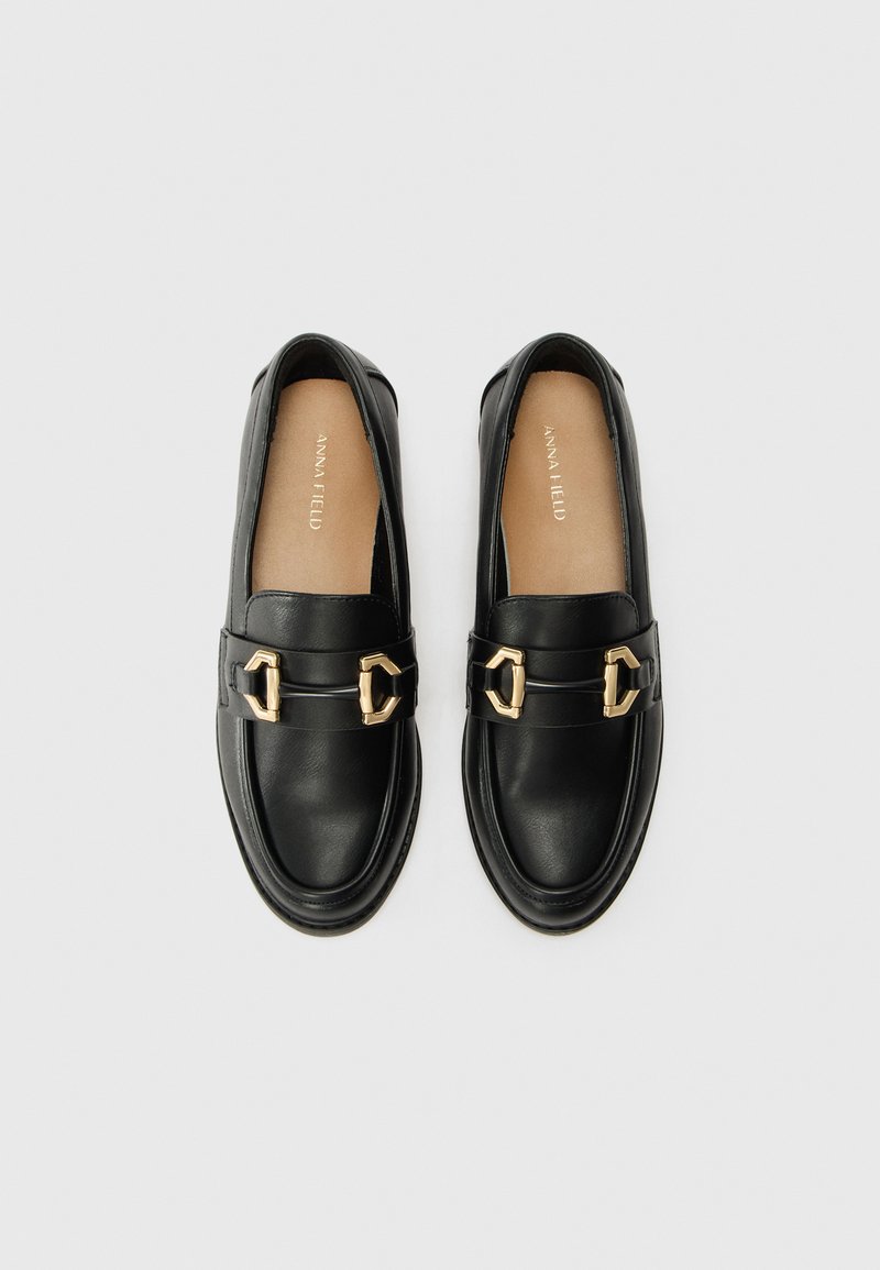 Mocasines de cuero negro con una textura suave, que cuentan con acentos de herrajes en tono dorado y un diseño de punta redondeada. Nombre de la marca en la plantilla.