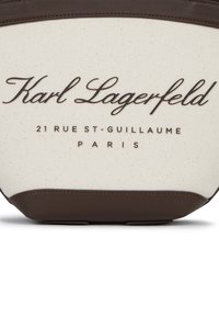 Kangas kott, mille kreemjas keha on pruuni nahkdetailidega ning peal on reljeefne tekst: "Karl Lagerfeld, 21 Rue St-Guillaume, Pariis."