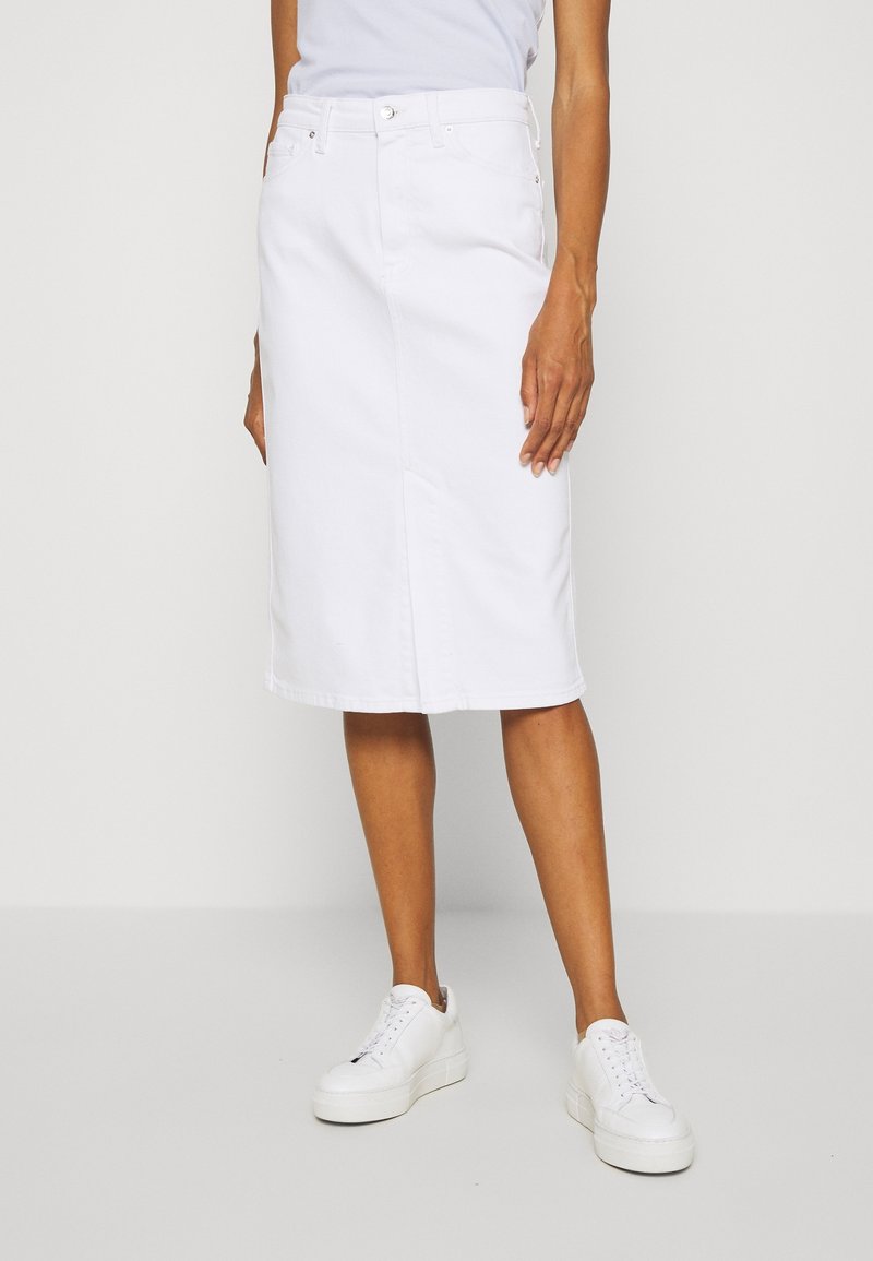 Falda midi de denim blanco con corte recto, dos bolsillos delanteros y pasadores para cinturón, combinada con zapatillas blancas. Textura suave, diseño minimalista.