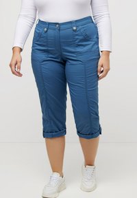 Pantalons blancs raccourcis en tissu doux, dotés de poches avant, de coutures visibles et d'ourlets retournés, associés à des baskets blanches.