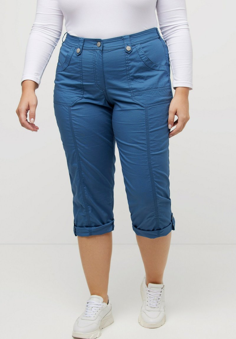 Pantalons blancs raccourcis en tissu doux, dotés de poches avant, de coutures visibles et d'ourlets retournés, associés à des baskets blanches.