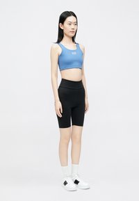 Kék crop top logóval, fekete magasderekú biciklis rövidnadrággal párosítva. A modell fehér, fekete részletekkel díszített tornacipőt és fehér zoknit visel.