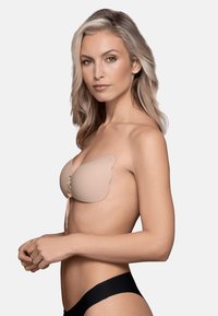 Nude liimabra, millel on lainelised servad ja nöörimisega esikujundus. Sile tekstuur, ühendamata välimus ja minimalistlik stiil.