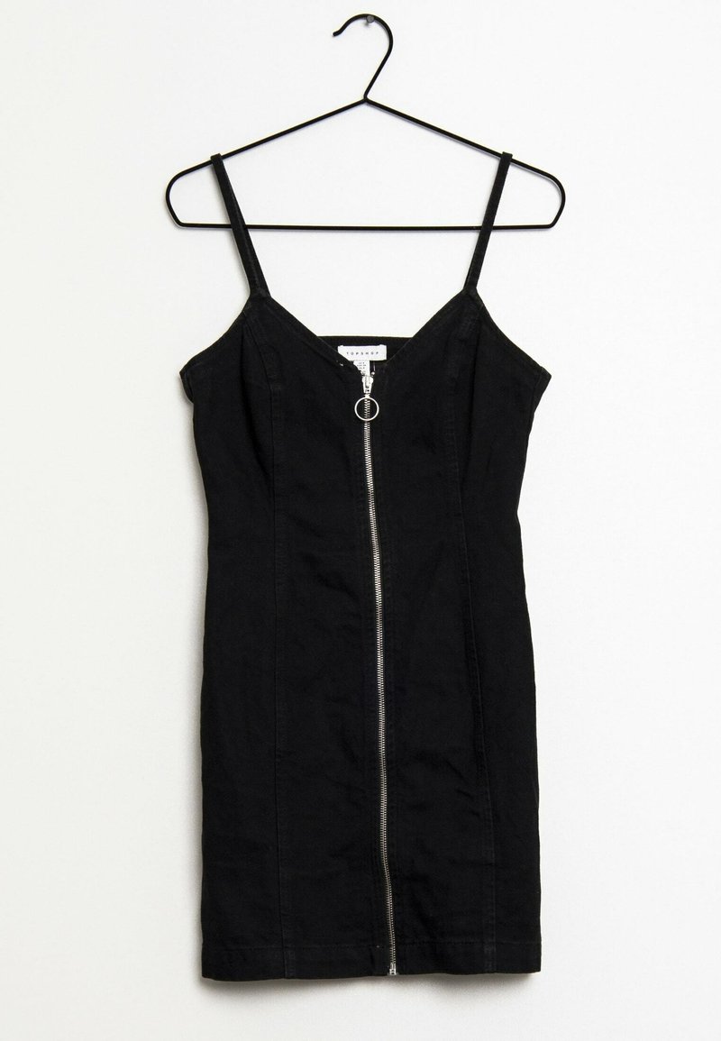 Mini-robe noire sans manches avec fines bretelles et fermeture éclair à l'avant, suspendue à un cintre noir sur un fond blanc.