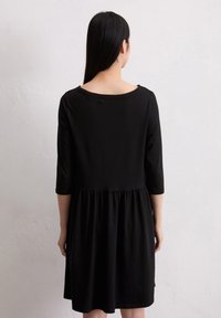 Zwarte jurk tot de knie, gemaakt van zachte stof, met een geplooide taille, driekwartmouwen en een brede halslijn.