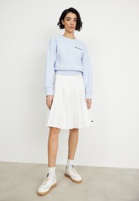 Light blue sweatshirt with black embroidery, white pleated skirt, and white sneakers with beige accents. Minimalistic design and casual styling.