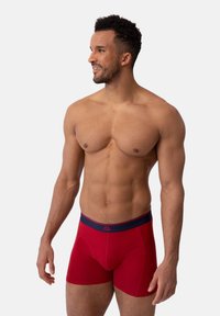 Boxer shorts rojos con una banda elástica en azul marino. Están hechos de una tela suave, con un diseño ajustado y una textura lisa.