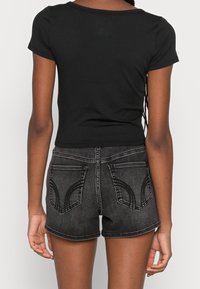 Zwarte geribbelde top met korte mouwen, gecombineerd met grijze denim shorts met gebogen achterzakken en een rafelige zoom.