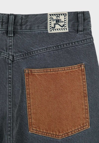 Baksidan av mörkgrå jeans med en kontrasterande brun denim bakficka och en sydd etikett som visar en stiliserad löpande figur.