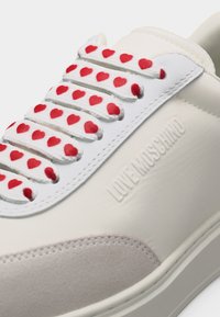 Λευκό αθλητικό παπούτσι με κορδόνια με κόκκινα μοτίβα καρδιάς και το λογότυπο «LOVE MOSCHINO» ανάγλυφο στο πλάι, με γκρίζες σουέτ λεπτομέρειες στην περιοχή των δαχτύλων.