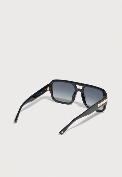 Μαύρα ορθογώνια γυαλιά ηλίου με φακούς με σκούρο διαβαθμισμένο χρώμα και χρυσή λεπτομέρεια στο μπράτσο, τοποθετημένα σε γωνία σε λευκό φόντο.