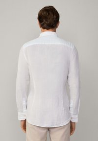 White long-sleeve shirt made of lightweight fabric. Features a classic collar, button cuffs, and a curved hem with a subtle texture.