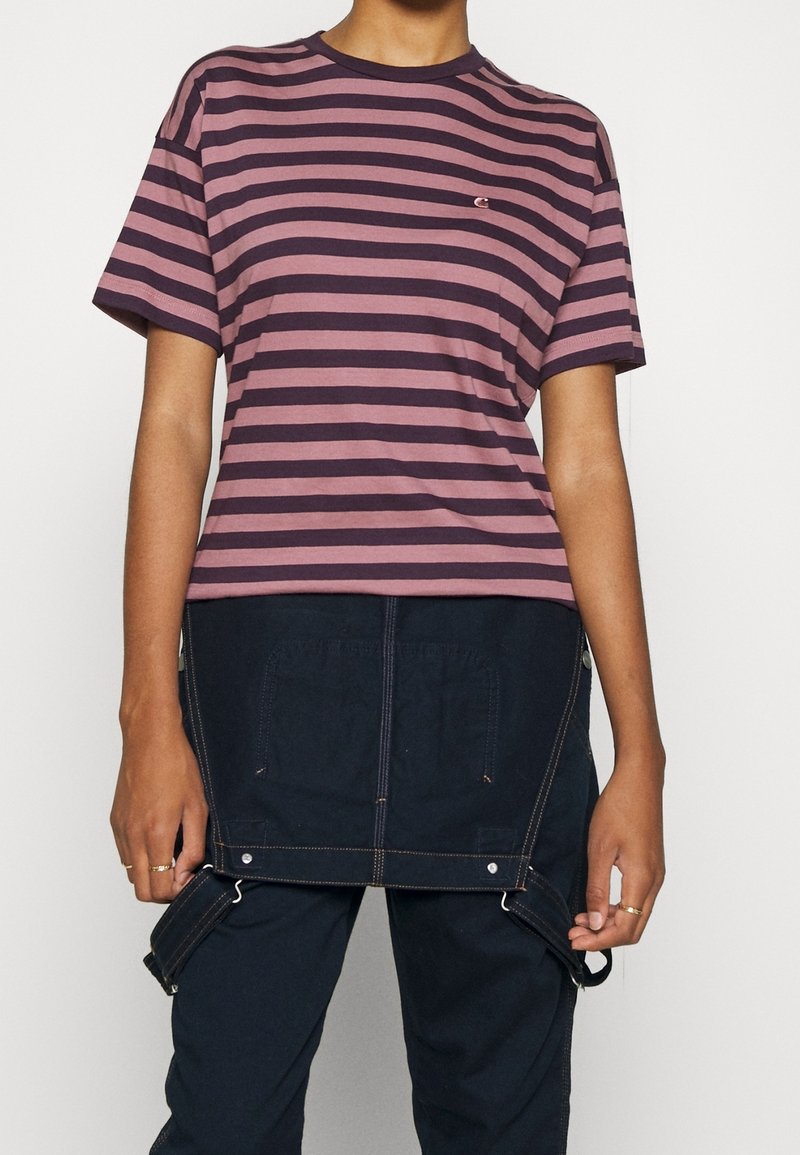 Stribet t-shirt i mauve og marineblå. Korte ærmer, rund halsudskæring, afslappet pasform. Båret med mørkeblå overalls med lommer og justerbare stropper.