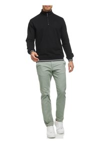 Svart hettegensar med glidelås og ribbestrikket krage og mansjetter, kombinert med lysegrønne chinos og hvite joggesko. Uformell, tettsittende design.