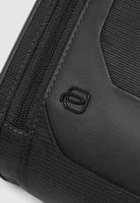 Bolso negro con textura que presenta costuras reforzadas, una cremallera suave y un logo de la marca en la esquina. Construido con materiales duraderos.