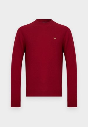 Red, round-neck sweater, made of smooth knit material. Features long sleeves and a small gold logo accent on the chest.