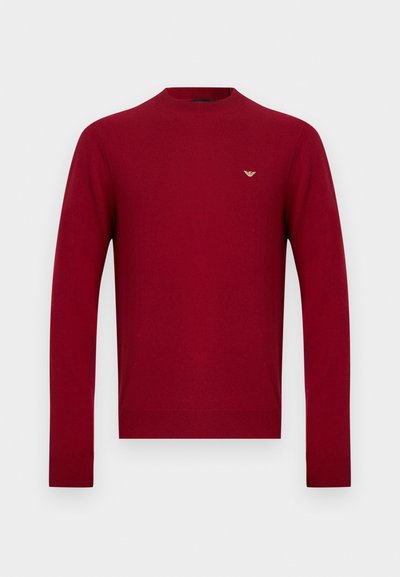 Pull rouge à col rond, en maille lisse. Comprend des manches longues et un petit logo doré sur la poitrine.