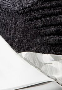 Schwarzer gestrickter Sneaker mit strukturiertem Obermaterial, weißer Sohle und camouflagemuster Akzenten an der Ferse. Glatte Oberfläche mit modernem Design.