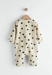 Beige corduroy jumpsuit met zwarte stippen, lange pofmouwen, elastische manchetten en een ronde halslijn. Ontworpen met een knoopsluiting aan de achterkant.