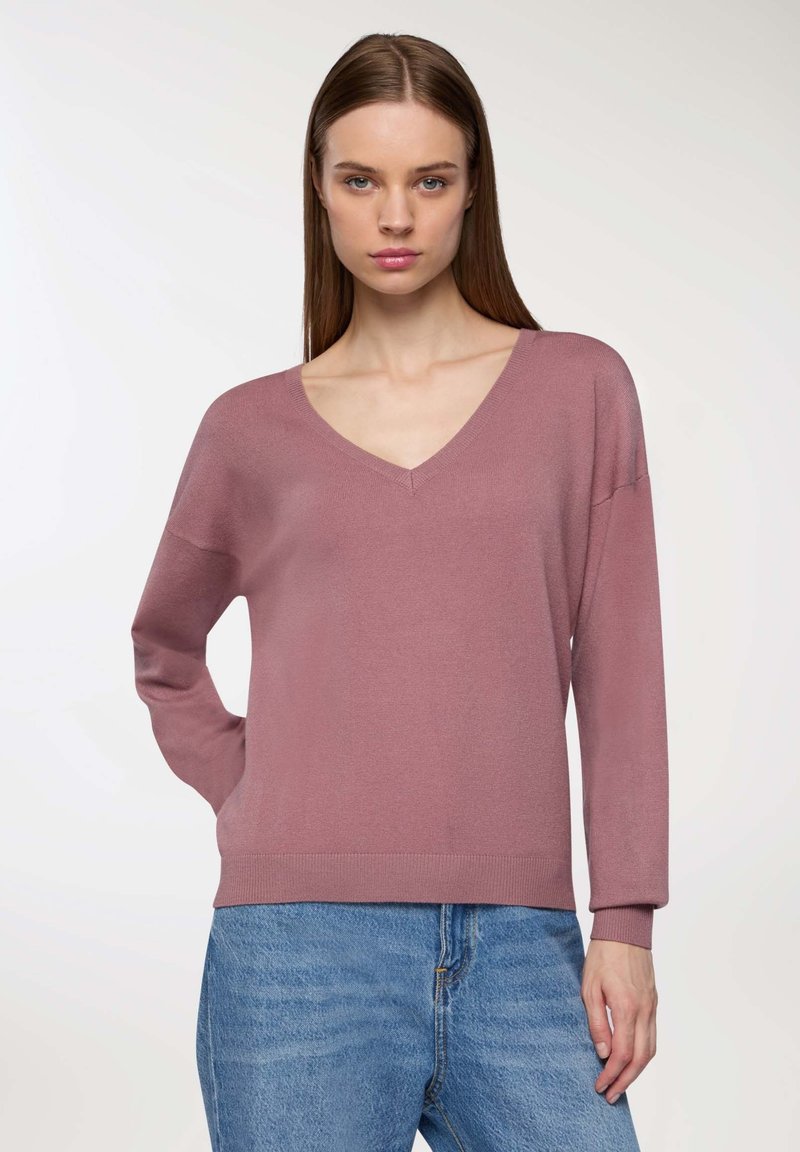 Maglione a V, con maniche lunghe in morbido tessuto rosa, caratterizzato da polsini e orlo a coste, abbinato a jeans blu casual. Texture liscia, vestibilità rilassata.
