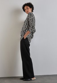 Blusa a righe in bianco e nero con vestibilità ampia e maniche a tre quarti, abbinata a pantaloni neri a gamba larga e scarpe nere con dettagli in pelliccia.