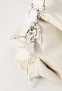 Borsa a mano in pelle bianca con superficie strutturata, hardware in argento e un charm a forma di cuore attaccato a una tracolla.