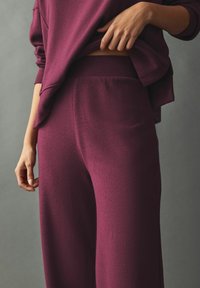 Bordo set za opuštanje od teksturiranog, mekog materijala. Gornji deo slobodnog kroja i hlače širokih nogavica s elastičnom tafom. Minimalistički dizajn.