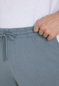 Jasnoniebieskie spodnie dresowe z elastycznym pasem i regulowanym sznurkiem. Gładka faktura, dopasowany krój, z bocznymi kieszeniami.