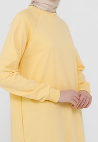 Sudadera amarilla de corte relajado, con puños acanalados y cuello redondo. Fabricada en una suave tela texturizada. Con aberturas laterales para mayor comodidad en el movimiento.