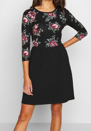 Musta mekko, jossa kolme neljäsosaa pitkät hihat, bodyn pinkki- ja vihreä kukkakuvio ja kerrostettu helma. Pehmeää, joustavaa materiaalia.