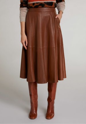 Jupe midi en cuir marron assortie à des bottes hautes en cuir, portée avec un pull à imprimé léopard beige.