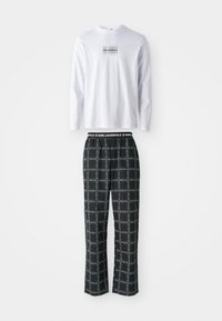 Cămașă albă cu mâneci lungi, având un grafic logo negru, asortată cu pantaloni de pijama negri cu carouri, care au o talie elastică și un model discret în carouri.