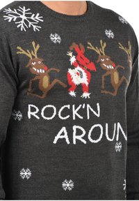 Pull en tricot gris foncé avec motifs festifs de rennes et du Père Noël, ornés de flocons de neige blancs et texte "ROCK'N AROUN".