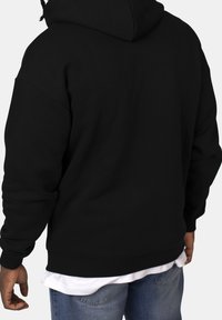 Sudadera negra con capucha, de corte relajado, con puños y dobladillo acanalados, hecha de un material suave. Llevada sobre una camiseta blanca y jeans azules.