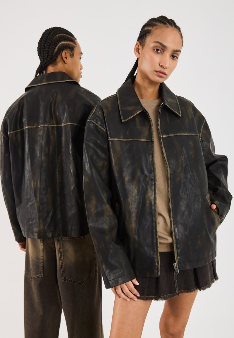 Veste en cuir noir avec une finition usée et des coutures visibles. Dispose d'un col pointu, d'une fermeture éclair et d'une coupe oversized.