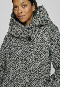 Gray and black patterned coat with a large hood, featuring a button closure at the neck and a textured, thick fabric.