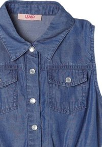 Camicetta senza maniche in denim azzurro chiaro con colletto classico, due tasche sul petto e bottoni argentati lungo la parte anteriore. Texture morbida e finitura liscia.