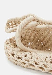 Panier rond tissé en coton beige avec un motif texturé. Poignées épaisses et lisses en boucle sur le bord, améliorant la prise en main et la structure.