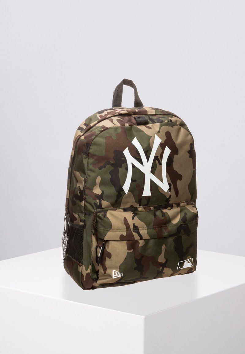 Mochila de camuflaje con logo blanco "NY", material de tela, compartimentos dobles con cremallera, bolsillo de malla lateral y asa de transporte superior.