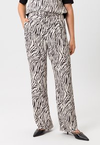 Hoge taille, wijde broek in crèmekleurige stof met een zwart zebra-strijkpatroon. Inclusief zak en een gladde textuur. Zwarte puntige schoenen.