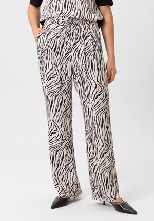 Hoge taille, wijde broek in crèmekleurige stof met een zwart zebra-strijkpatroon. Inclusief zak en een gladde textuur. Zwarte puntige schoenen.