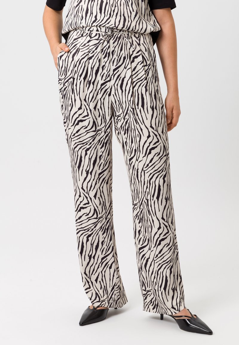 Hoge taille, wijde broek in crèmekleurige stof met een zwart zebra-strijkpatroon. Inclusief zak en een gladde textuur. Zwarte puntige schoenen.