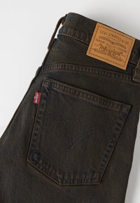 Σκούρο τζιν Levi's που δείχνει την πίσω τσέπη με την χαρακτηριστική ραφή, την κόκκινη ετικέτα Levi's και την καφέ δερμάτινη ετικέτα της μάρκας στη μέση.