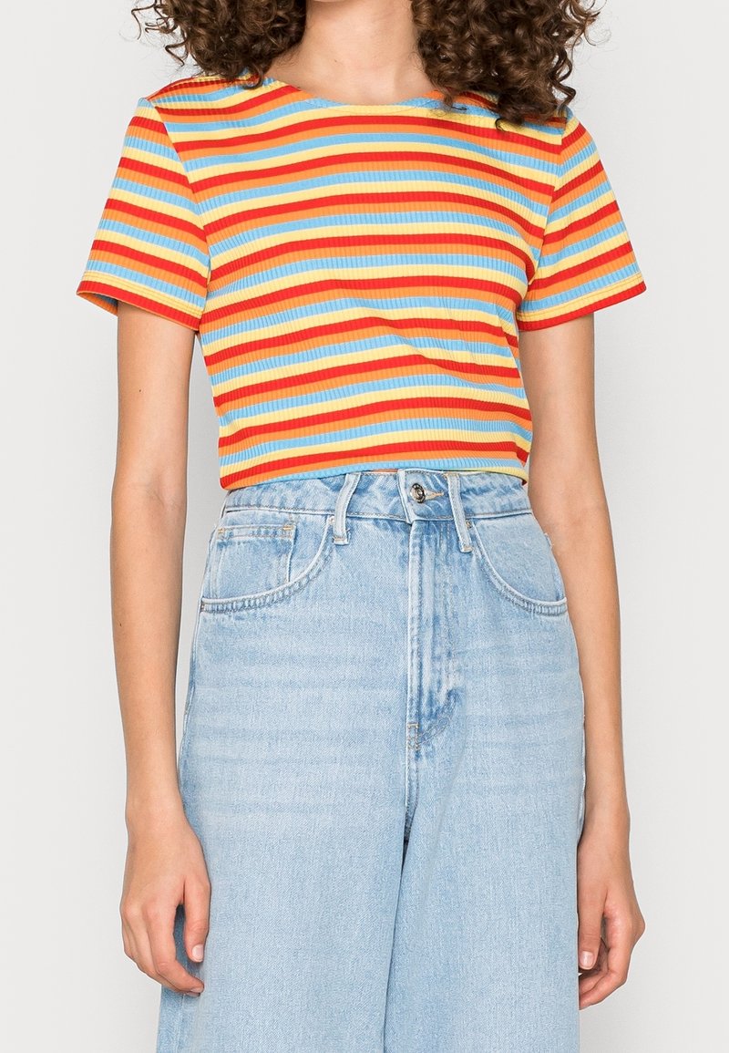 Personne portant un haut côtelé à manches courtes avec des rayures horizontales rouges, orange, jaunes, bleu clair et blanches, associé à un jean taille haute bleu clair.