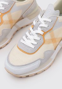 Zapatillas ligeras con parte superior de malla en beige y gris, con acentos en naranja, cordones blancos y una suela acolchada.