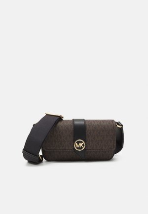 Petit sac bandoulière marron compact avec sangle en cuir noire et fermoir logo MK doré sur le rabat avant, sur un fond clair uni.